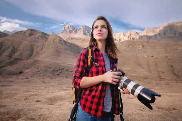 Молода приваблива біла жінка з професійною фотокамерою в руках на тлі епічних високих скель у кавказьких горах. Фототури та ландшафтна фотографія — стокове фото