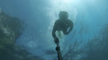 Maskeli, yüzgeçli ve derin dalış yapan genç bir adam suyun altında yüzüyor..