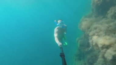 Maskeli, yüzgeçli ve derin dalış yapan genç bir adam suyun altında yüzüyor..