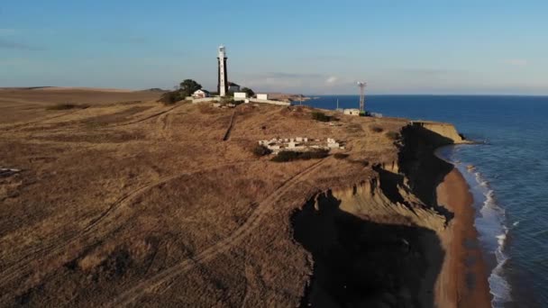 半島の岬に黒と白の縁を持つ未知の灯台の空中ビュー。鍵が低い。フィルム・グレイン — ストック動画