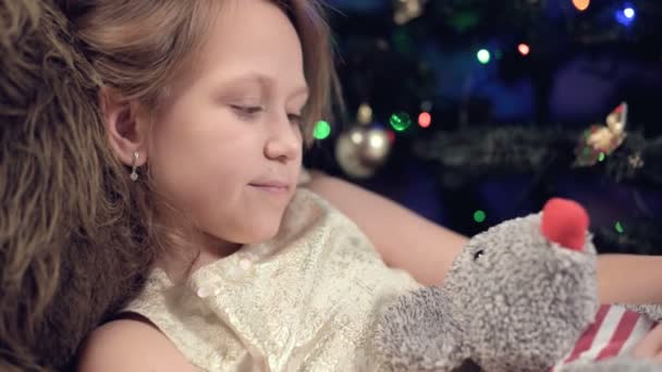 Jahr der Ratte. Glückliches kaukasisches Mädchen in der Nähe des Weihnachtsbaums, das eine Spielzeugratte umarmt. vor dem Hintergrund der blinkenden Lichter des Weihnachtsbaums — Stockvideo