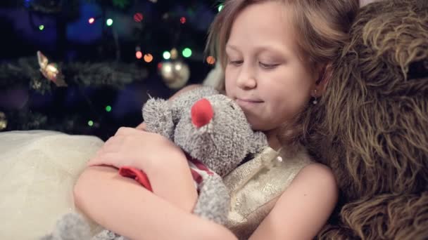 Rok krysy. Šťastný kavkazský dítě dívka poblíž vánočního stromečku objímající krysa. na pozadí blikajících světel vánočního stromku — Stock video