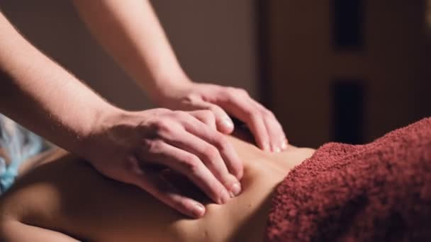 Un joven masajista masculino hace un masaje profesional cliente chica en un salón de masajes profesional con velas encendidas en una habitación oscura — Vídeos de Stock