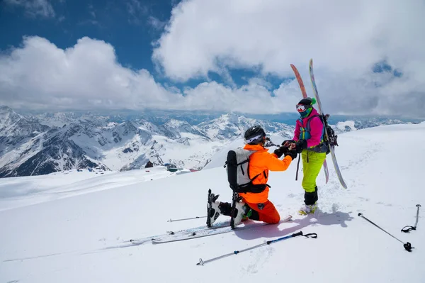 Um homem atleta esquiador freerider faz uma proposta para se casar com sua mulher esquiador alto nas montanhas no inverno. contra o pano de fundo de picos cobertos de neve. Proposta de casamento em condições extremas — Fotografia de Stock