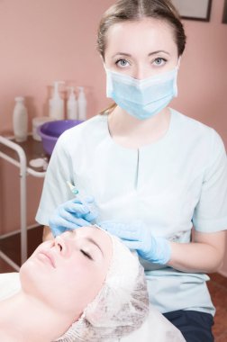 Güzellik uzmanı kameraya dolgu malzemesi ya da takviye için bir şırınga gösteriyor. Doktor hasta için kozmetik işlemler yapar. Kozmetik Kliniği Sağlık Hizmetleri. Hyaluronik asit