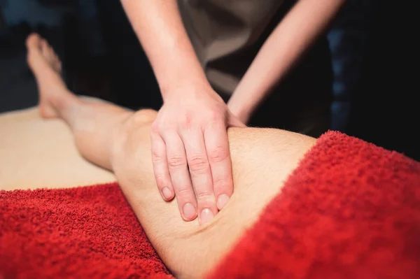Massagem esportiva da coxa para um homem em um salão de massagem profissional com luz contrastante — Fotografia de Stock