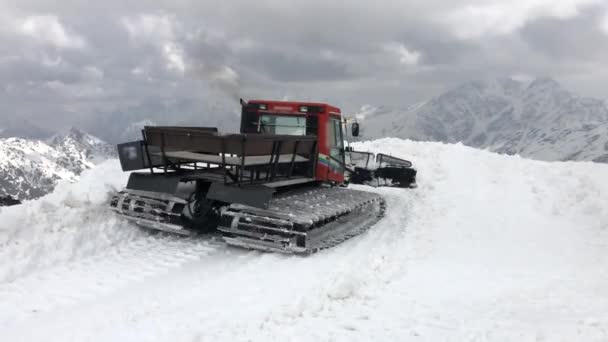 Червоний трактор 4K Snowcat на гірськолижному курорті розчищає сніг протягом дня. На тлі засніжених гір — стокове відео
