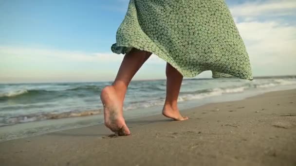 Nogi młodej kobiety w zwolnionym tempie chodzącej boso po plaży. Pozostawienie śladów na piasku Turysta na wakacjach nad morzem. Kobieta w pięknej, trzepoczącej sukience na wietrze — Wideo stockowe