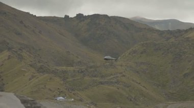 Mavi tanımlanamayan helikopter dağlarda bulutlu havada uçuyor.