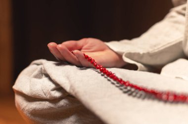 Meditasyon yapan bir keşişin erkek eli, mum ışığında karanlık bir odada kırmızı bir tespih tutar. Pratik ve aydınlanma