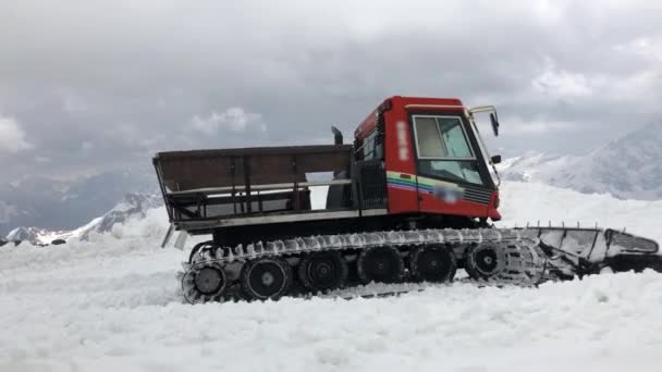 Ein roter 4K-Snowcat-Traktor in einem Skigebiet räumt tagsüber Schnee. Vor dem Hintergrund schneebedeckter Berge — Stockvideo