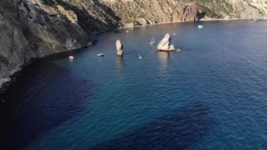 Tek tek kayaların ve yüksek kayalıkların yanındaki teknelerin deniz kıyısındaki hava manzarası. Lüks Akdeniz tatilleri
