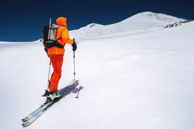 Sırt çantası, buz baltası, kayak ve direkleri olan bir dağcı Elbrus Dağı 'na bir kayak turuna çıkıyor. Taşra ve serbest kayak konsepti
