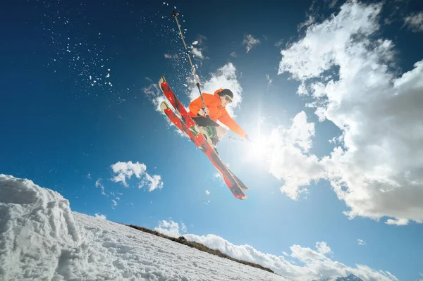 A young man skier in sunglasses and shorts makes a jump trick on a background of blue sky and clouds. motion blur — Stock Photo, Image