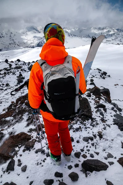 Portret van een mannelijke atleet skiër van achteren met een rugzak en ski 's op de achtergrond van de hoge bergen van de Kaukasus. Backcountry skitouren en freeride — Stockfoto