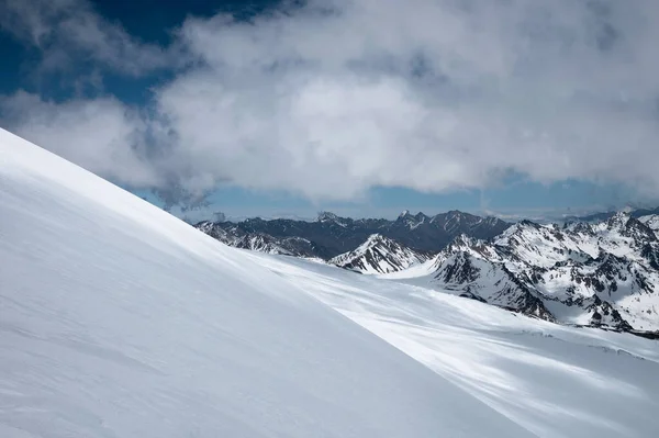 Berglandschap besneeuwde helling op een zonnige dag tegen de achtergrond van hoge bergen — Stockfoto