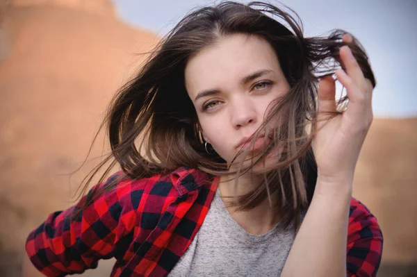 Retrato de uma jovem caucasiana atraente em uma camisa vermelha quadriculada contra um fundo de montanhas. Felicidade e prazer nas montanhas. O vento sopra seu cabelo — Fotografia de Stock