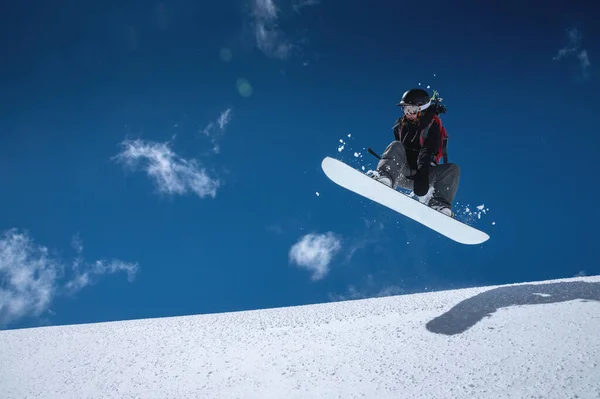 Γυναίκα αθλητής snowboarder κατά την πτήση μετά το άλμα σε μια χιονισμένη πλαγιά με φόντο ένα σκούρο μπλε ουρανό — Φωτογραφία Αρχείου