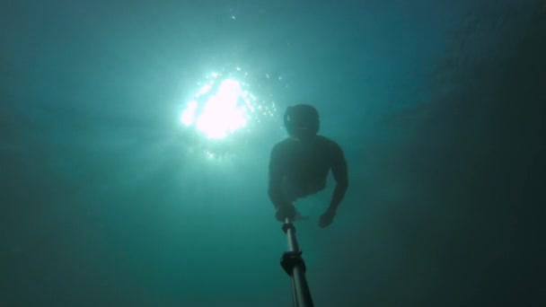 Человек в чистой морской воде занимается подводным плаванием и фридайвингом. Силуэт водолаза, плавающего в глубине с лучами солнца сзади. Фильм зерно в видео — стоковое видео