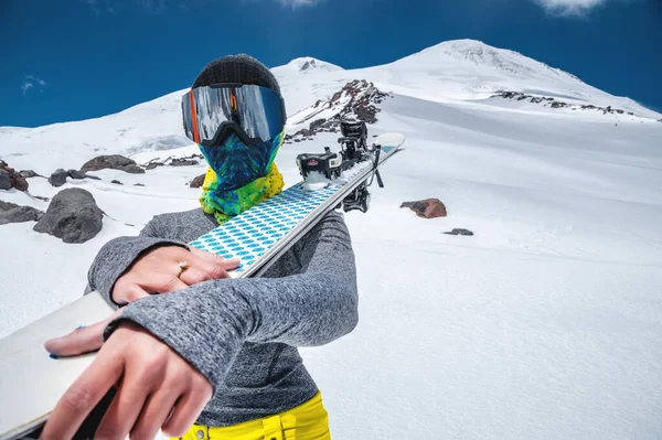 Μια κοπέλα σκιέρ στέκεται με σκι στον ώμο της στο φόντο του χιονισμένου βουνού Έλμπρους στη βόρεια Καυκάσια. — Φωτογραφία Αρχείου