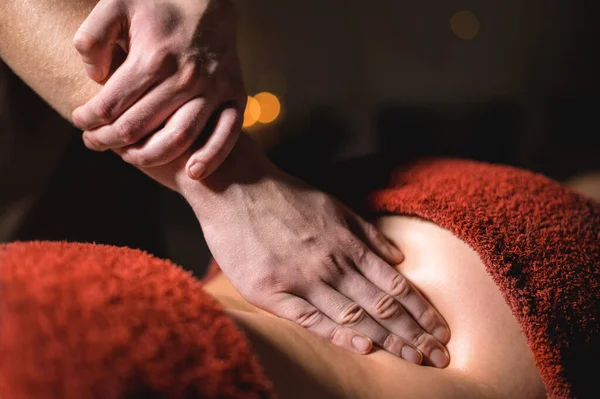 Primo piano di un uomo che fa un massaggio lombare a una cliente donna in una stanza buia di una sala massaggi spa — Foto Stock