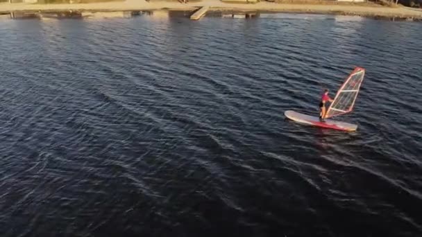 Bir rüzgar sörfü tahtası uçurmayı öğrenen genç bir kadının havadan görünüşü. Gün batımı egzersizi. Alçak tuş — Stok video