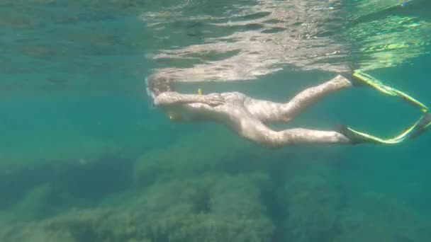 En kvinde i en gul badedragt med snorkelmaske og finner svømmer over et koralrev på en solrig dag, skudt i slowmotion. – Stock-video