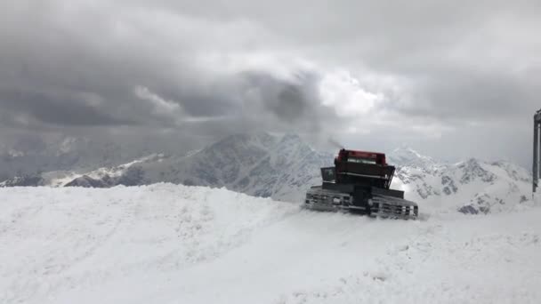 Червоний трактор 4K Snowcat на гірськолижному курорті розчищає сніг протягом дня. На тлі засніжених гір — стокове відео