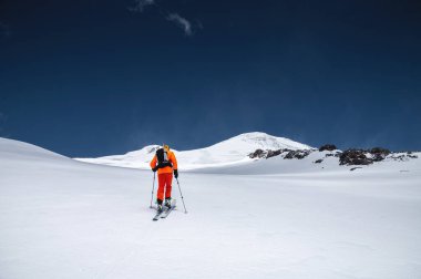 Sırt çantası, buz baltası, kayak ve direkleri olan bir dağcı Elbrus Dağı 'na bir kayak turuna çıkıyor. Taşra ve serbest kayak konsepti