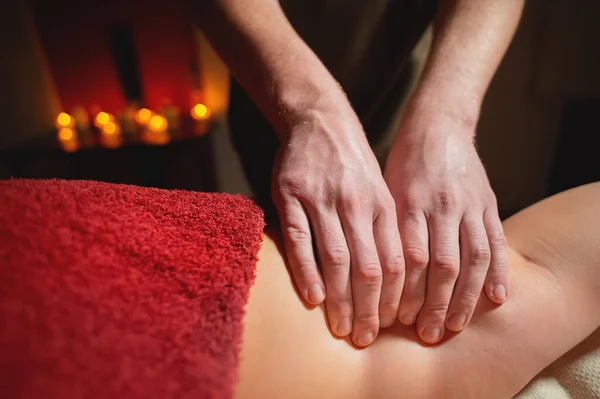 Male masseur doing massage of the knee to a woman patient in a dark room of a spa salon — Stock Photo, Image