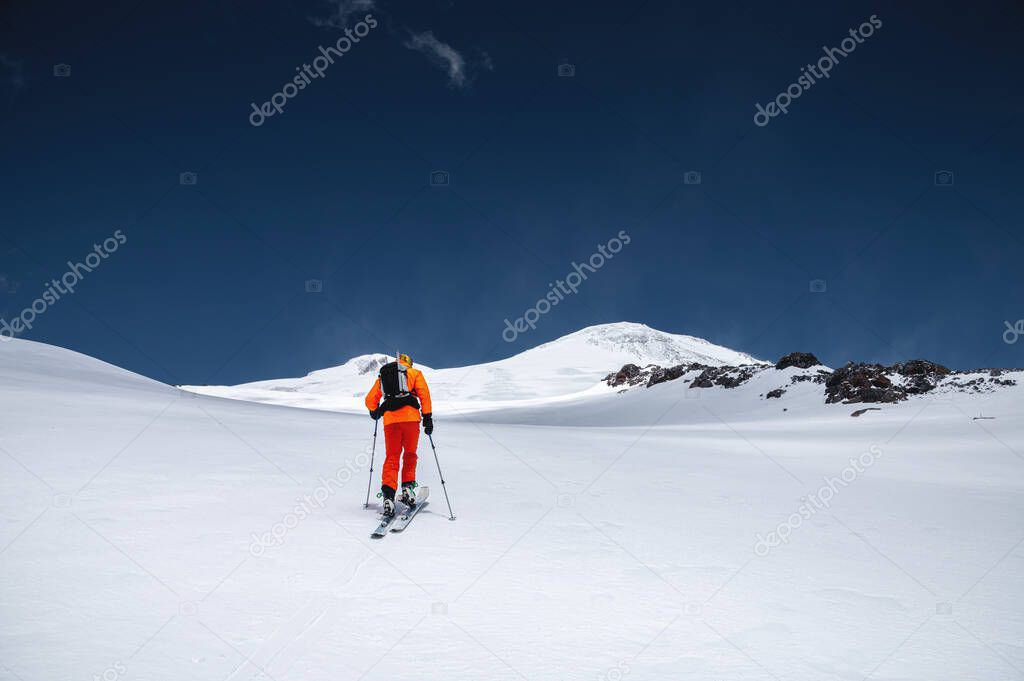 A mountaineer skier with a backpack, an ice ax, skis and poles, ascend on a ski tour to Mount Elbrus. Backcountry and freeride skiing concept
