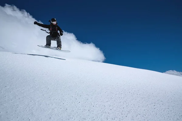 Γυναίκα αθλητής snowboarder κατά την πτήση μετά το άλμα σε μια χιονισμένη πλαγιά με φόντο ένα σκούρο μπλε ουρανό — Φωτογραφία Αρχείου