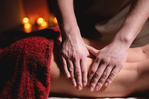 Male masseur doing massage of the knee to a woman patient in a dark room of a spa salon — Stock Photo, Image
