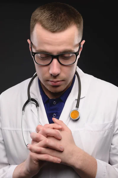 Портрет несчастного молодого врача со стетоскопом с головной болью на тёмном фоне. Проблемы с медиком — стоковое фото