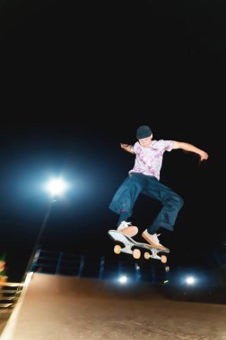 Genç kaykaycı geceleri kaykay parkında atlama numarası yapıyor.