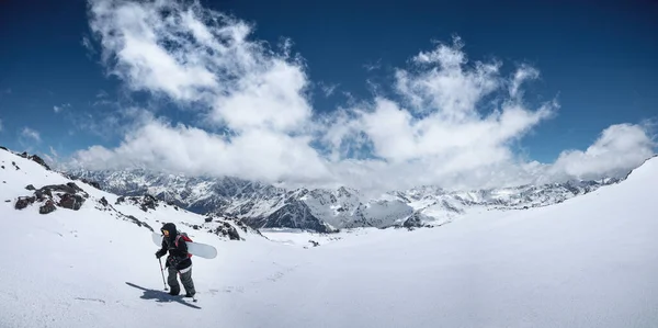 Mulher snowboarder freerider subir a neve fresca equitação sertão. Picos de montanhas e céu azul com nuvens no fundo — Fotografia de Stock