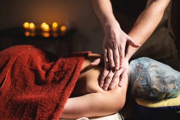 Man sterke handen massage terug naar middelbare leeftijd vrouw in donkere spa kamer door kaarslicht — Stockfoto