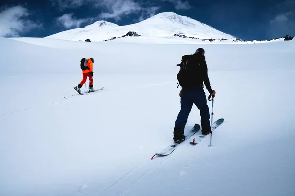 Two freeride skiers climb up the fresh snow in a ski tour. The summit of Mount Elbrus and the blue sky on the background — Stock Photo, Image