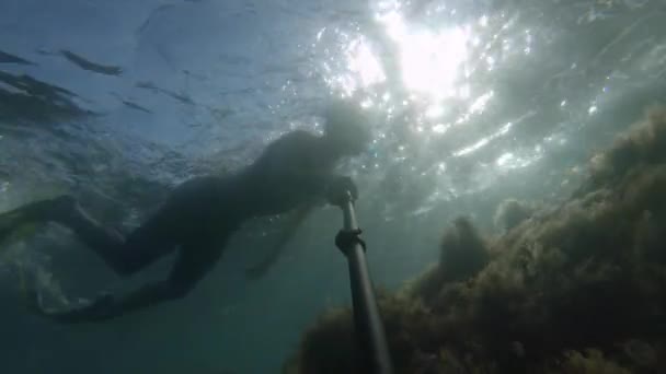 Mladý sportovec v masce a šnorchl plave se selfie klackem hluboko pod vodou. Slunce svítí do vody — Stock video