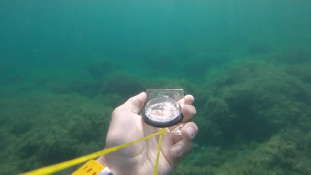 Widok pierwszej osoby męskiej ręki trzymającej plastikowy kompas magnetyczny obraca się z boku i szuka prawidłowego kierunku pod wodą. — Wideo stockowe