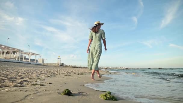 Donna attraente al rallentatore che cammina a piedi nudi lungo la spiaggia la mattina presto. Turista in abito verde chiaro su una spiaggia dorata — Video Stock