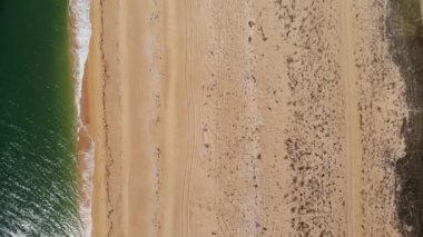 Okyanus mavi dalgalarının kumsala çarptığını gösteren hava manzarası. Deniz dalgaları ve kumlu kumsalın güzel havadan çekilmiş görüntüsü..