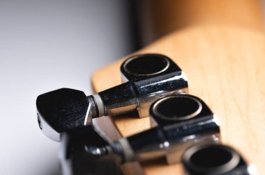 Gri arka planda akort mandalları ve telleri olan gitar panosu. Yakın plan.