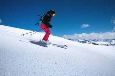 Kırmızı pantolonlu bir serbest kayakçı bulutlu bir havada karlı bir yamaçtan aşağı kayıyor. Kadınların serbest spor geçmişi