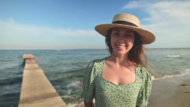 Portrait of a young caucasian beauty woman with the ocean in the background. Beautiful fashionable woman looking at the camera and smiling cheerfully in slow motion — Stock Video