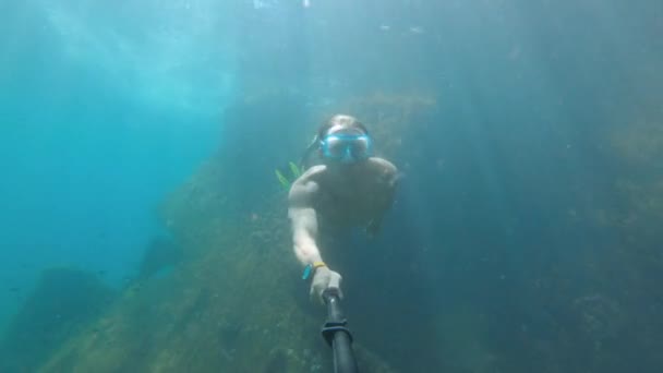 Ελεύθερη κατάδυση νεαρός άνδρας σε μια μάσκα κολυμπά κάτω από το νερό δίπλα σε ένα βυθισμένο σκάφος. Selfie stick κάμερα δράσης — Αρχείο Βίντεο