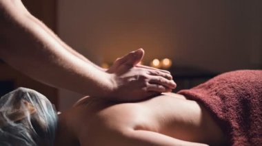 Sırtında ve belinde profesyonel masaj. Erkek masör bir müşterisine mum ışığında karanlık bir odada masaj yapar.