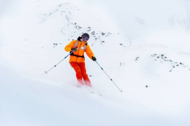 Turuncu kayak takımlı genç bir kayakçı görüş mesafesi düşük karlı bir dağ yamacına biniyor. Kötü hava kayağı konsepti