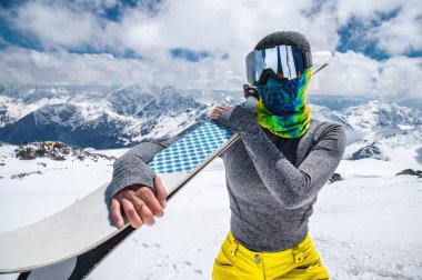İnce Müslüman bir sporcunun portresi kapalı bir yüzle ellerinde kayaklarla Kafkasya 'nın yüksek dağlarının arka planına yaslanmış.