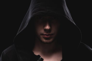 Kapüşonlu bir adamın silueti ya da siyah arka plandaki bir zorbanın. Alacakaranlıkta bir kanun kaçağının yüzü